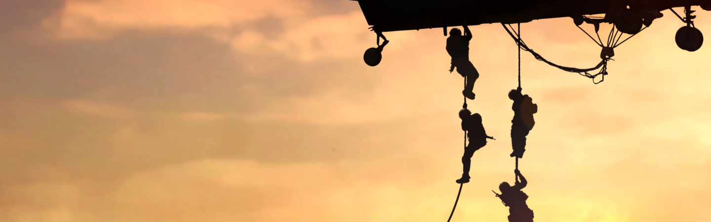 Military members scaling down a rope from a helicopter before they start their mission.