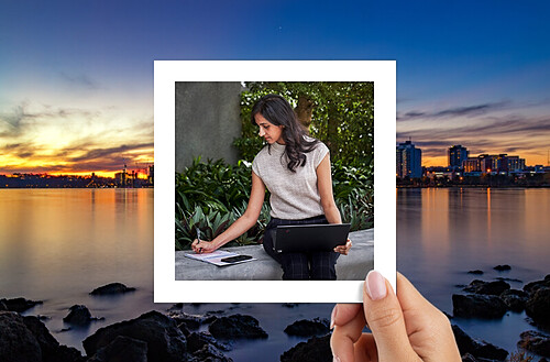 A hand holds a photo of a person in a headscarf with hot air balloons in the sky, against a backdrop of glass building reflections.