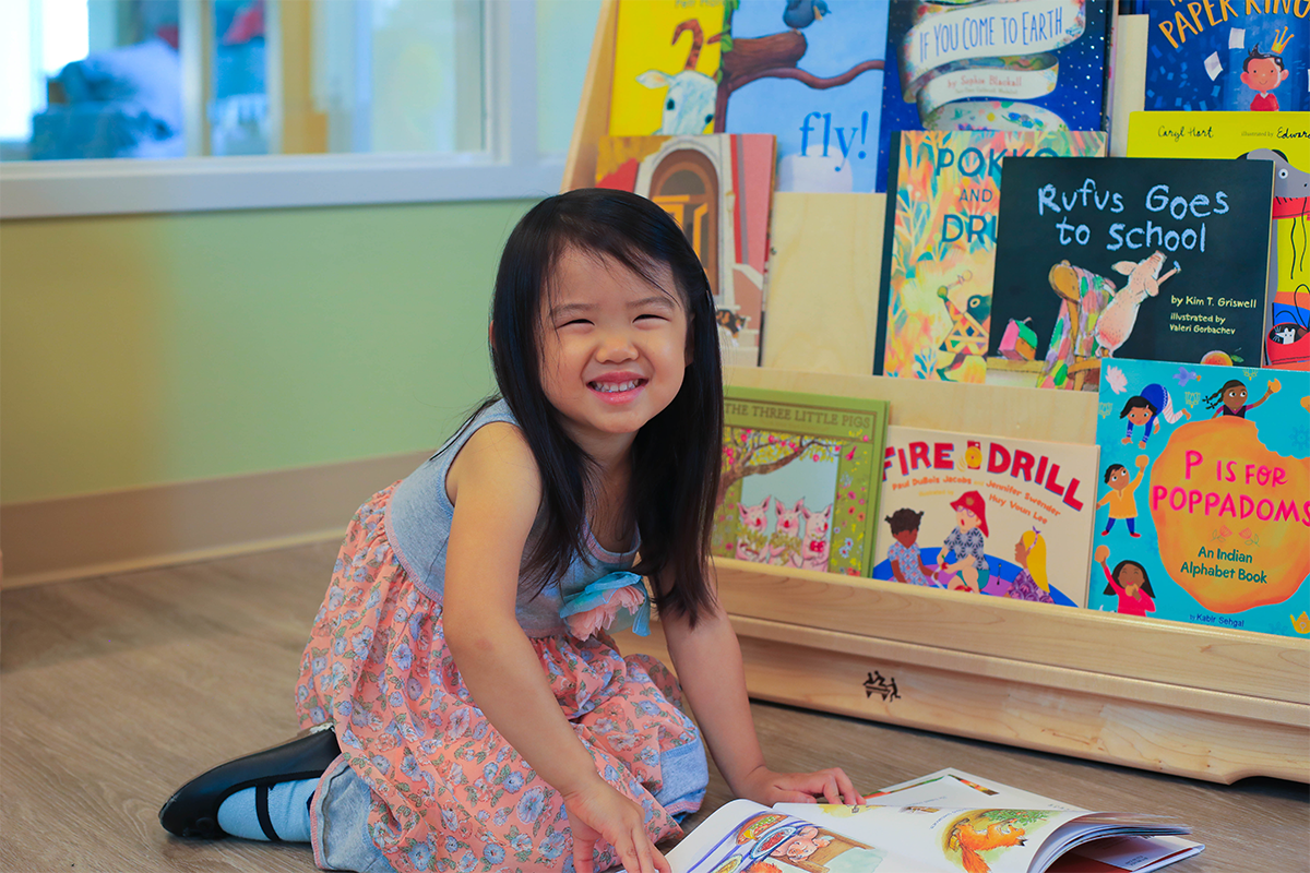 Child sitting on the floor reading a book in front of a colorful bookshelf.