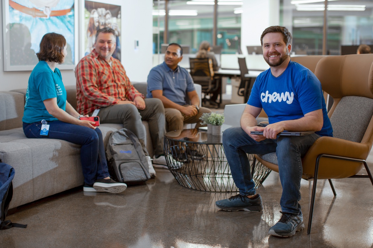 A white bulldog looking into the camera while being held by a Chewy team member