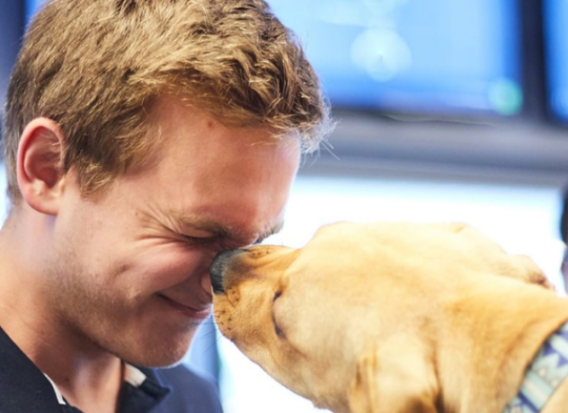 A Chewy team member squinting his eyes while getting kissed by a golden dog