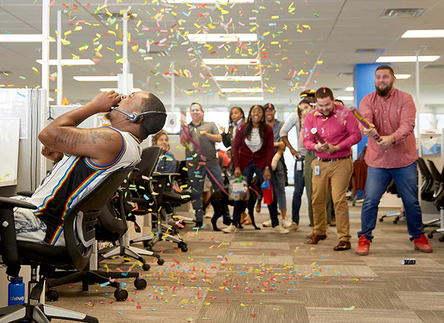 A group of Chewy team members surprising a fellow team member with a confetti cannon blast in celebration of a milestone