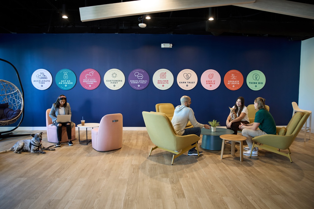 Three Chewy team members in neighboring cubicles, looking at their computer screens and laughing together