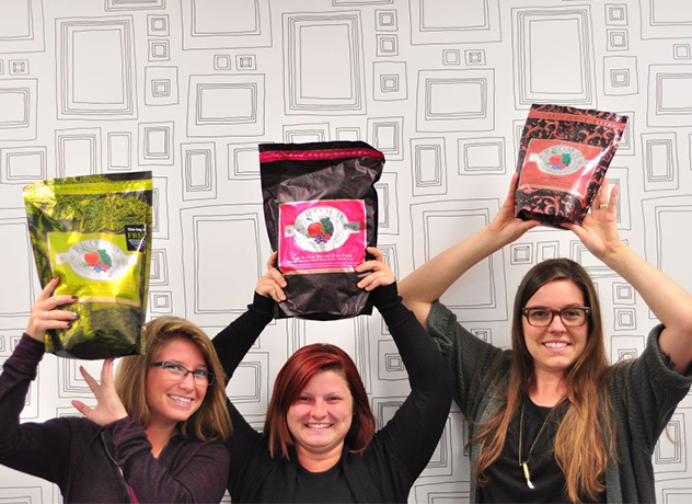 Three smiling Chewy team members looking at the camera and holding bags of dog food over their heads