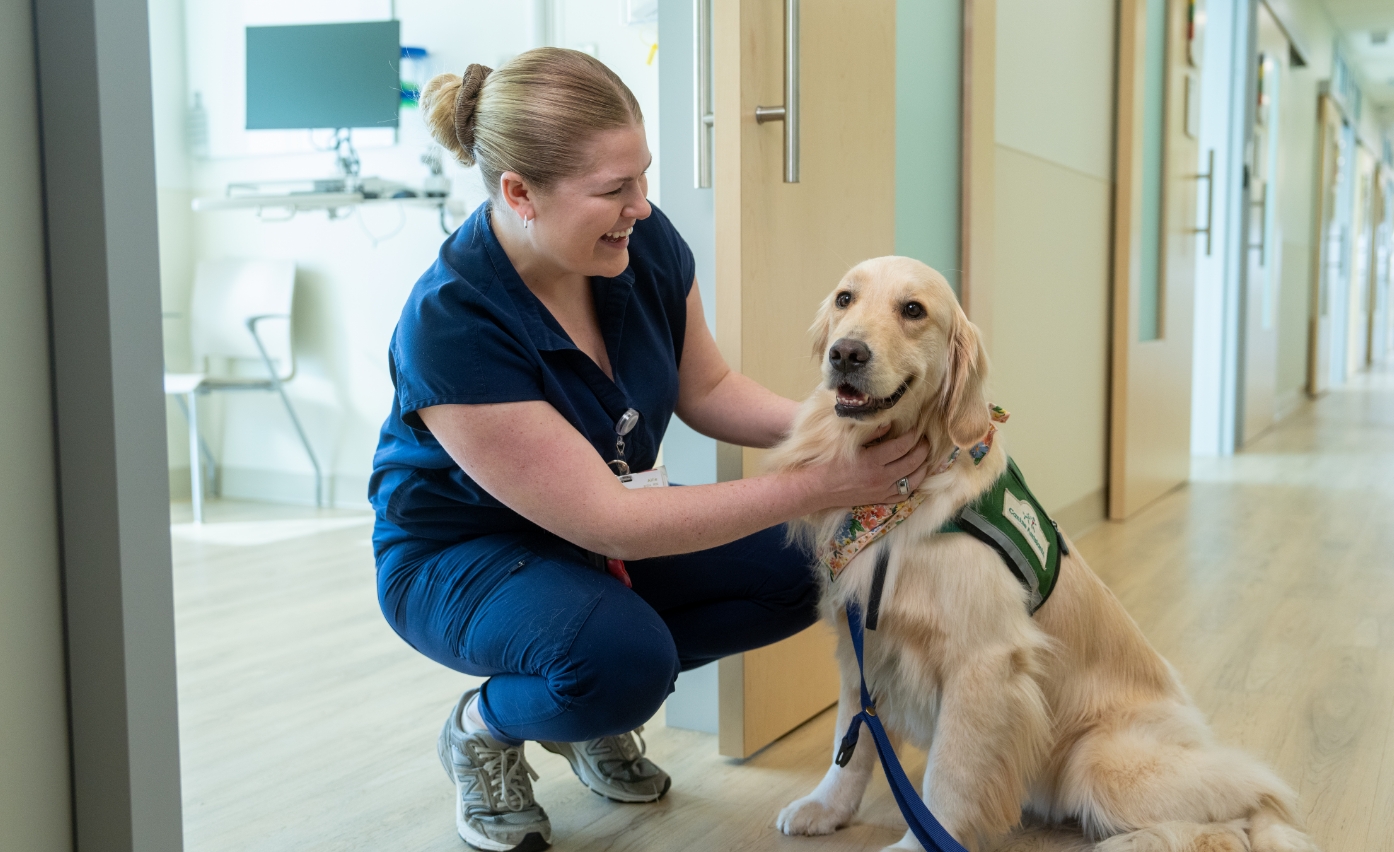 Children’s clinician pets hospital facility dog in clinical hallway. 