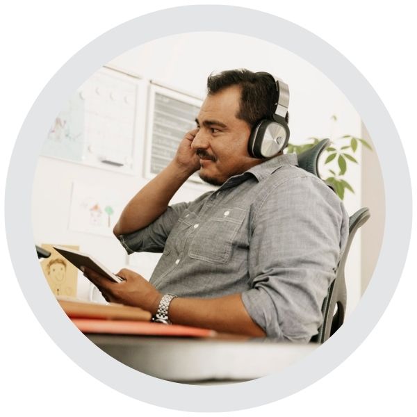 A person seated at a desk wearing headphones and using a tablet while working in a home office environment.