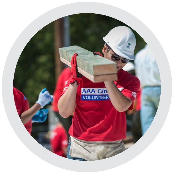 A volunteer wearing an AAA Cares shirt carrying building materials during a community service project