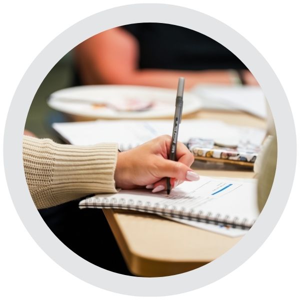  A person writing notes in a notebook while seated at a table during a meeting or workshop