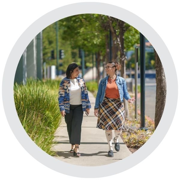 Two people walking together along a sidewalk in an urban neighborhood with trees and greenery