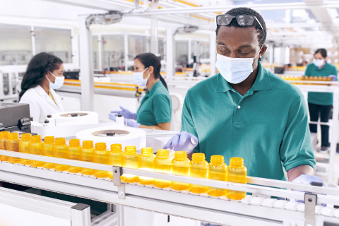The Cigna Group employees in a clean, organized facility wearing masks and gloves while handling prescription bottles