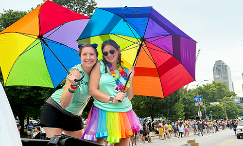 Two Pride ERG members holding umbrellas with the Pride colors