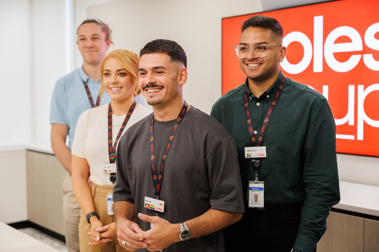 Four Coles graduates standing together posing for a photo in front of Coles Group banner