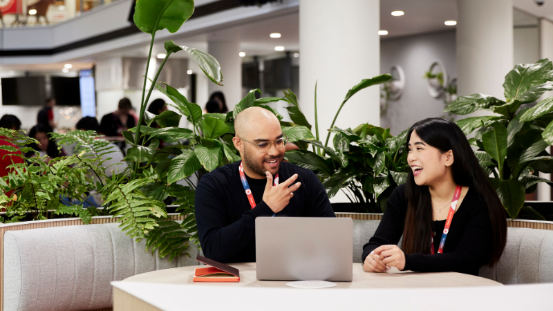 Two Corporate team members, male and female having a meeting in the Coles SSC. The background is filled with plants and team members