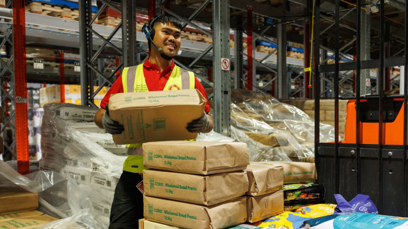 A male Coles employee safely unloading a pallet of stock in a warehouse
