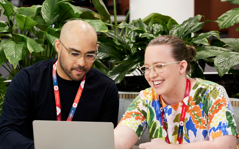 Two Coles team members sitting together and collaborating on a laptop in a modern workspace with green plants, reflecting an inclusive and supportive office environment.