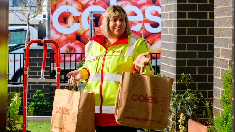 Female CFC team member wearing a red polo and green safety vest delivering two bags of groceries by the door at a house