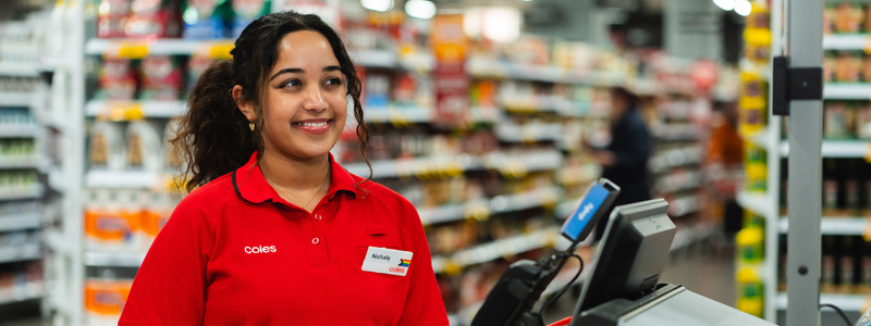 A young female team member smiling into the distance while working in the Coles self checkout are 
