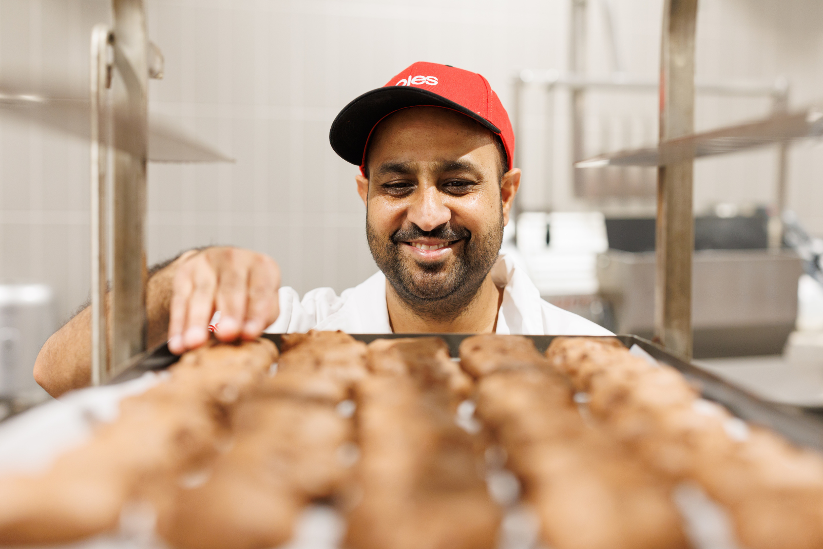 Male Coles Baker inspecting a tray of baked goods with a smile