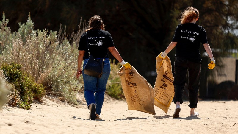 Two Coles Liquorland team members walking on a sandy beach carrying large hessian bags during a clean-up activity. The image represents environmental responsibility, teamwork, and Coles’ commitment to sustainability and community impact.