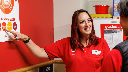 Female team member pointing to a Coles values poster in a supermarket tea room