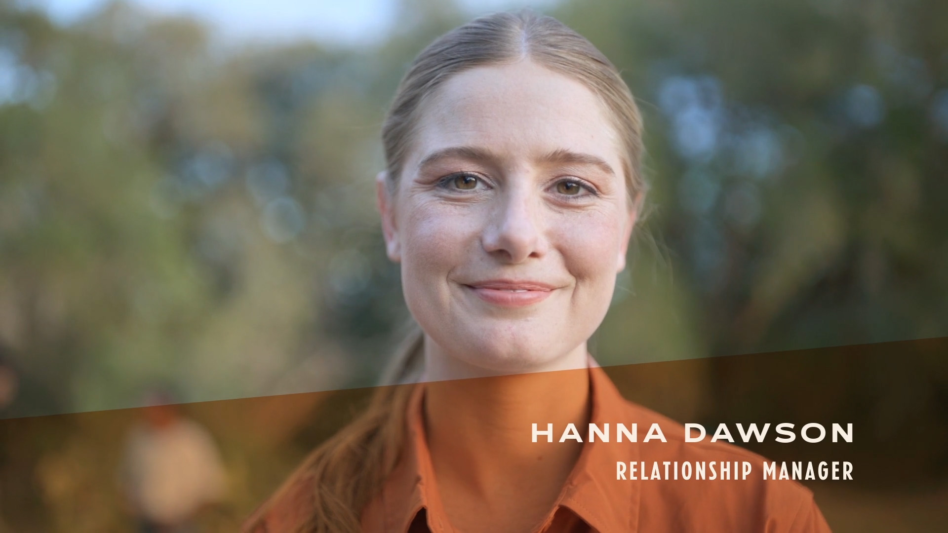 Initial video image of Hanna Dawson, Relationship Manager in a orange shirt in the woods