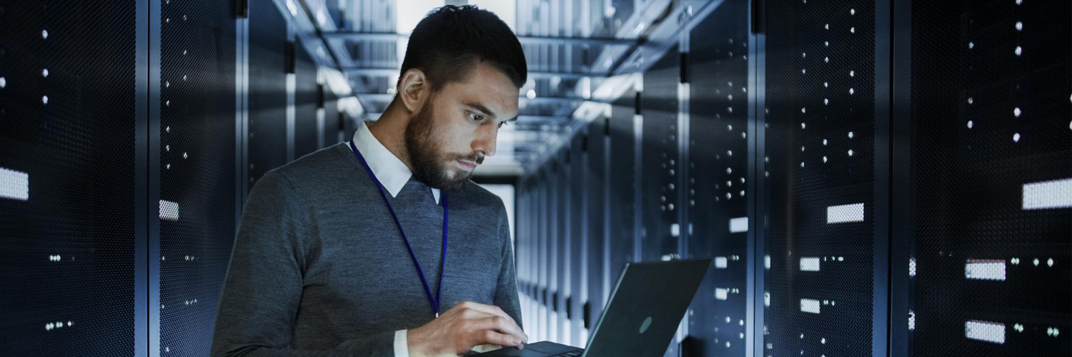 ITTechnicianWorksonaLaptopinBigDataCenterfullofRackServers