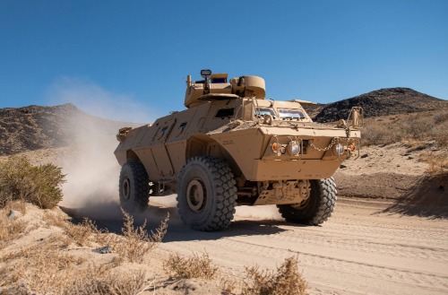 Tan armored tactical vehicle from Textron Systems driving on a desert off-road path.