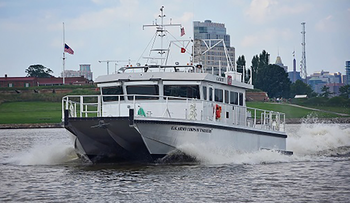 white ship steering through the water with buildings in the background