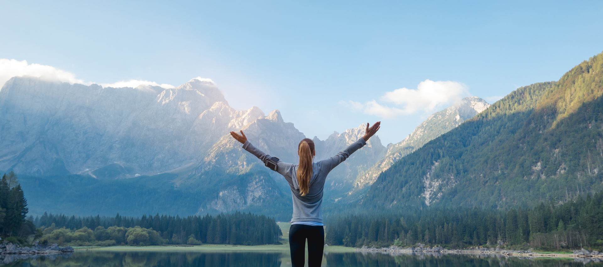 Life Time member embracing the outdoors in front of a lake and raising her hands up to the sky and mountain in front of her.
