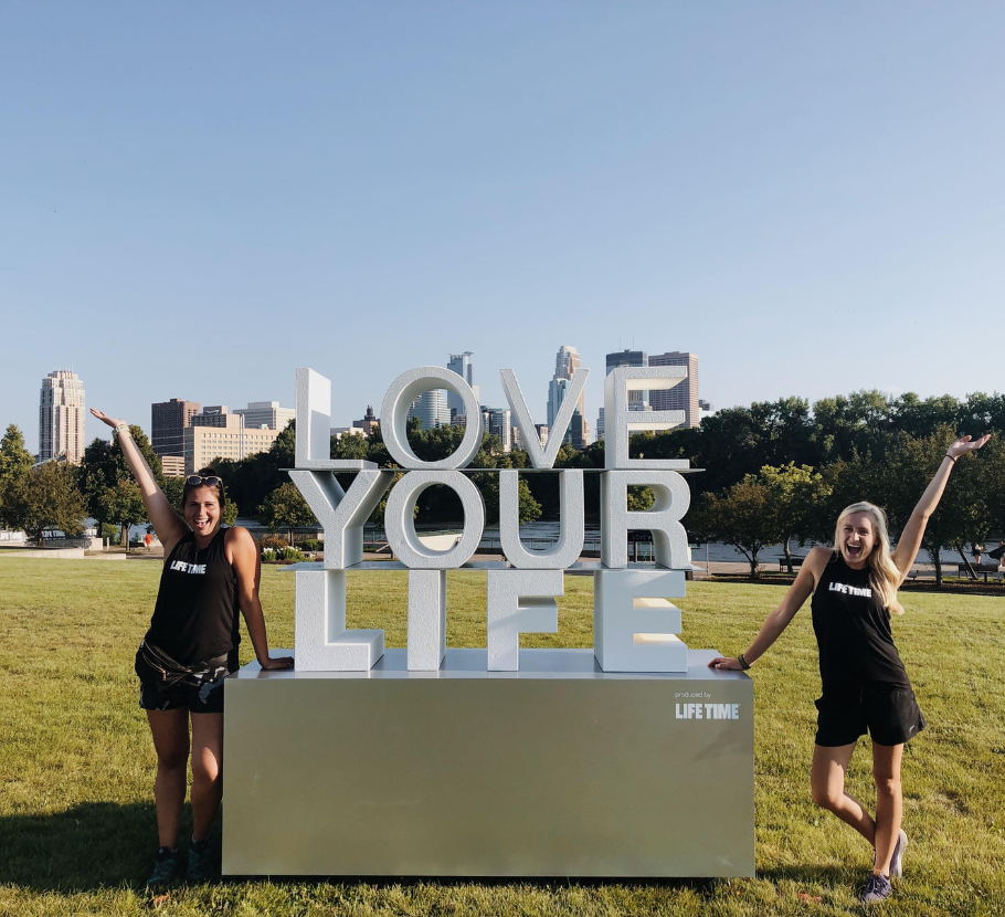 Life Time interns smiling with the outdoor Love Your Life sign.