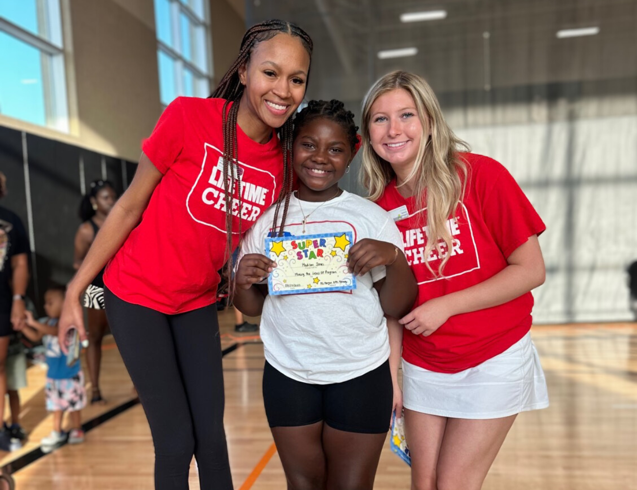 Life Time cheer team members smiling with a kid in their program.