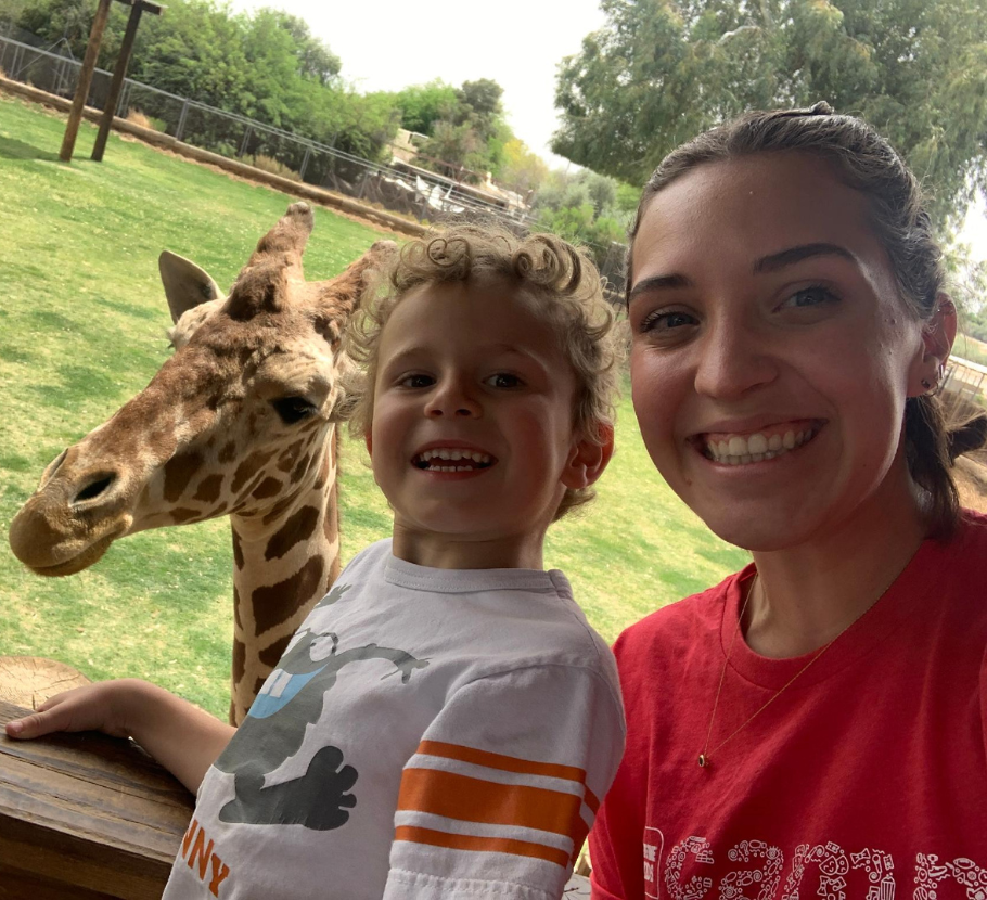 Life Time kids counselor and kid taking a selfie with a giraffe at the zoo.