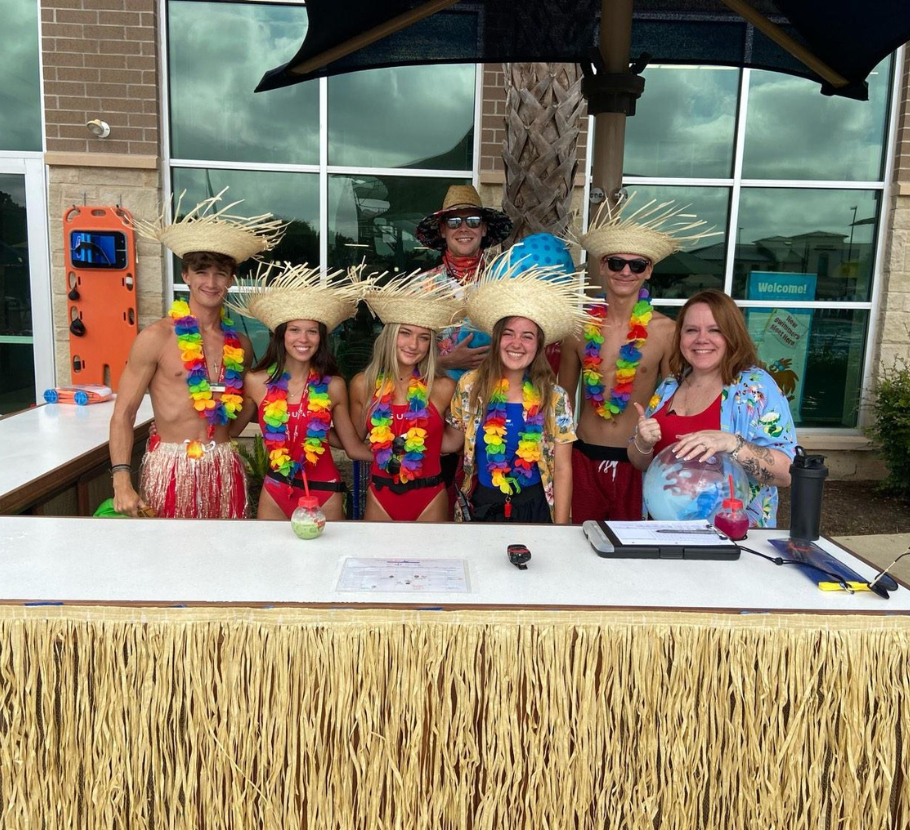 Life Time pool concierge and staff all smiling together wearing tropical gear, hats, and lei's.