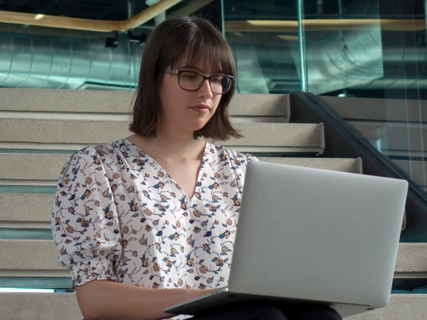 Female associate working on her laptop on the steps of the Tech Hub