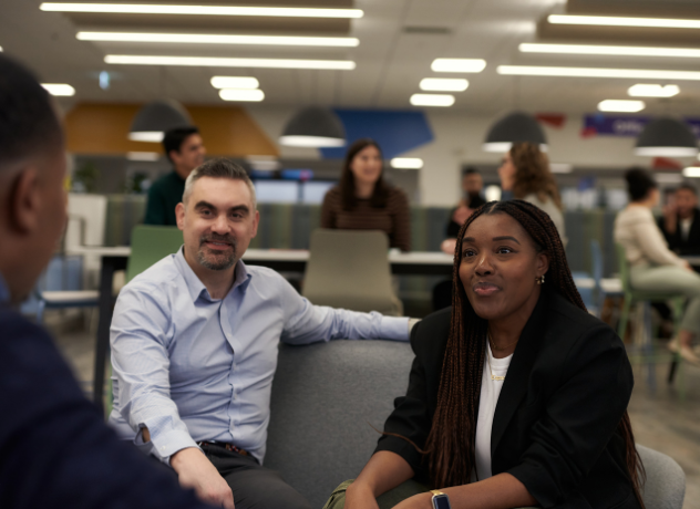 Image of two Associates sitting on a sofa, speaking to another Associate.
