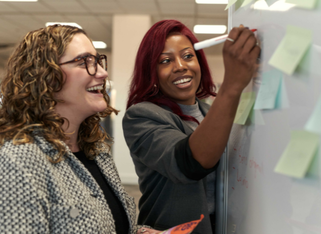 Picture of two Associates writing on a while board with sticky notes on.