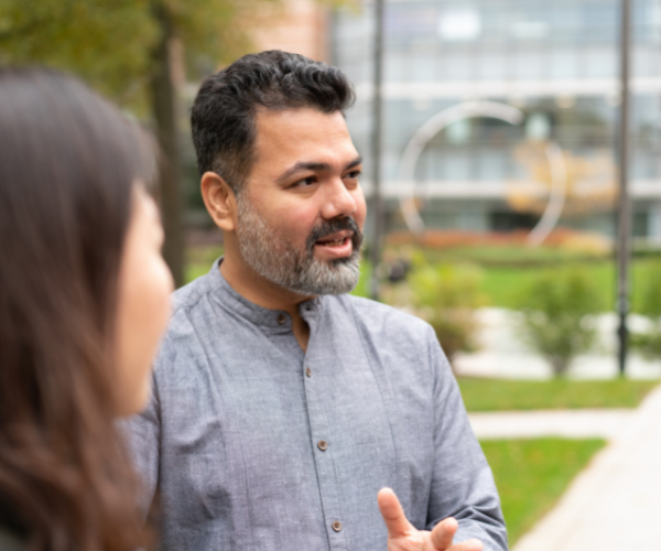 Man with beard and grey shirt talking to a woman outside