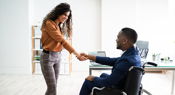 A photo of a woman shaking hands with a man sitting in a wheelchair. 