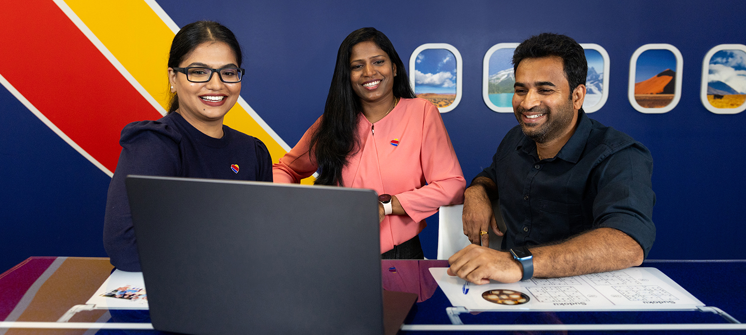 Three employees smiling while looking at a laptop