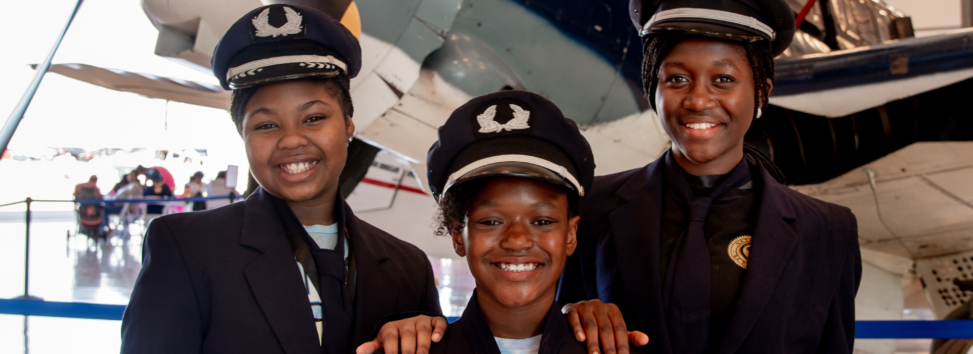 Three girls in Pilot uniforms smiling in front of a plane 