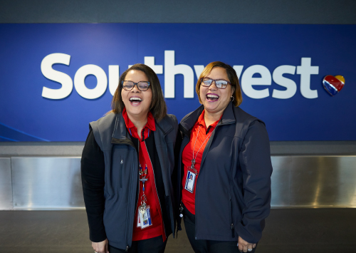 Two woman with their arms around each other and smiling in front of a Southwest logo