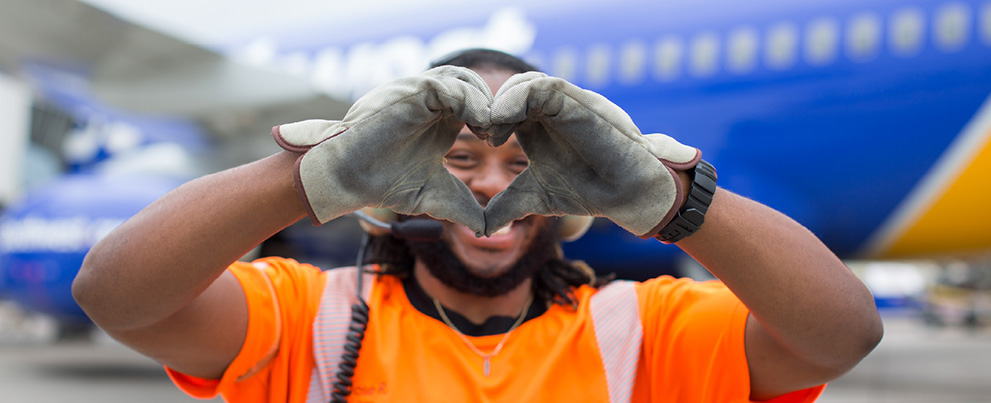 [1:15 PM] Ashley Black Southwest Ramp Agent smiling at the camera through his hands that are in the shape of a heart.