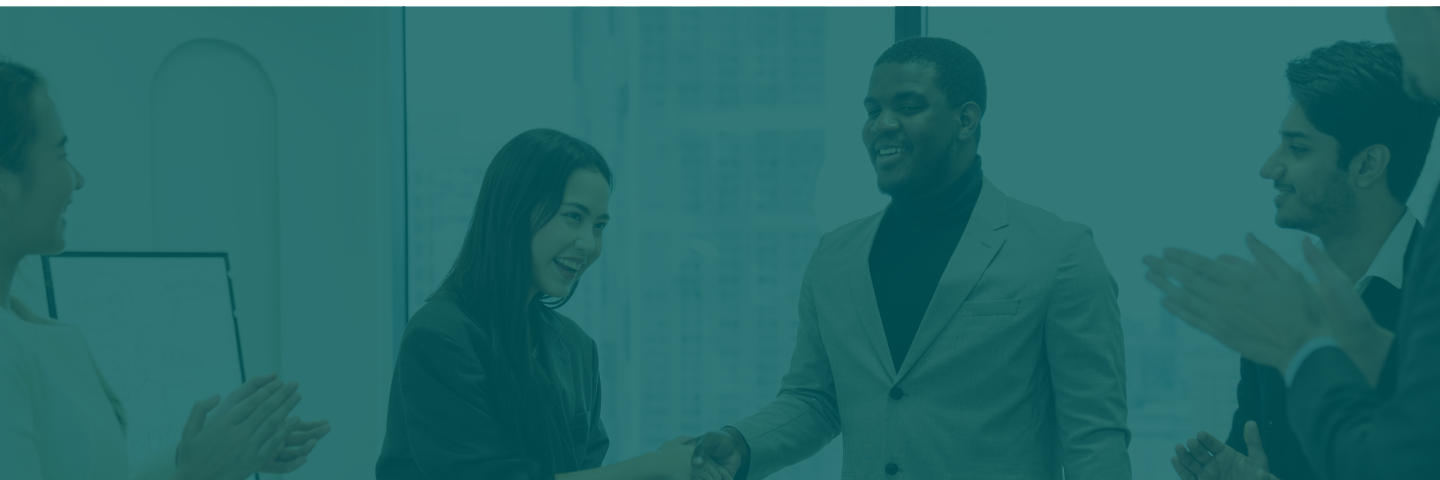 Woman and man shaking hands in meeting while coworkers applaud.