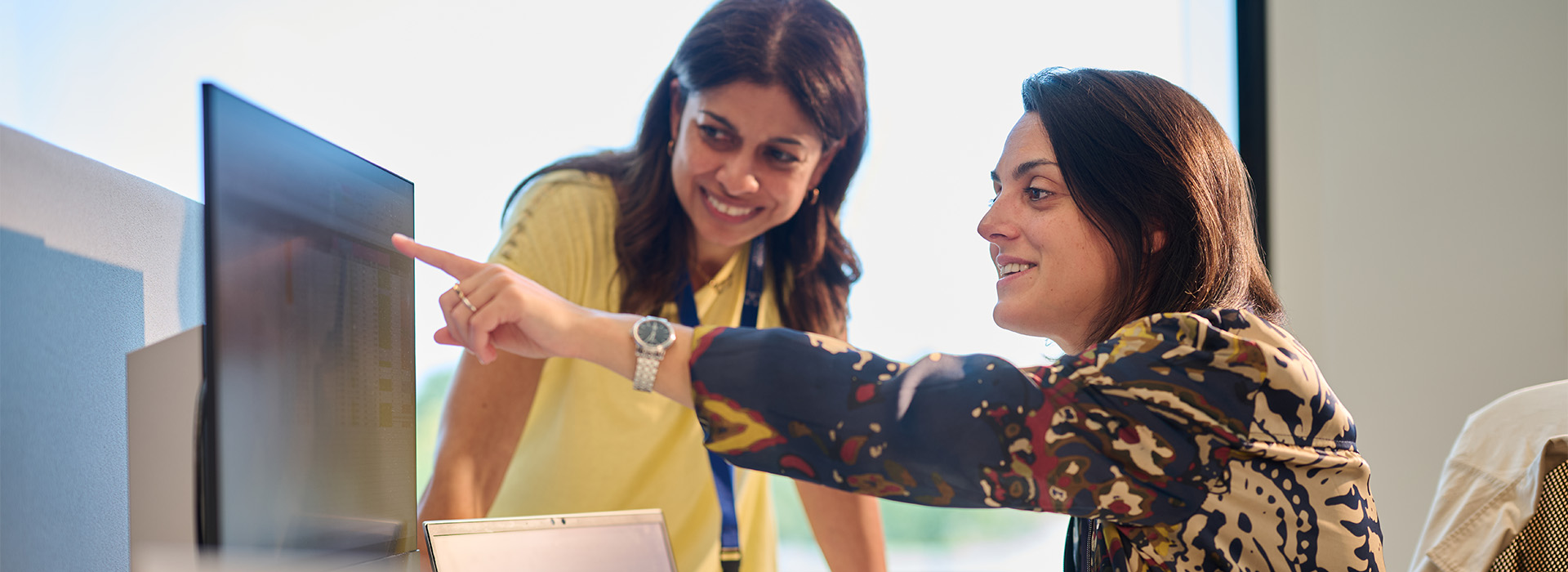 2 colleagues discussing and pointing to something on a desktop screen