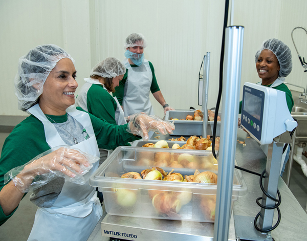 Four Veritiv employees wear aprons and hairnets volunteering at a food bank.