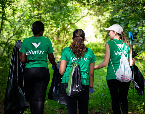 Three Veritiv employees wearing green shirts with the Veritiv logo on the back walking in the woods collecting litter.