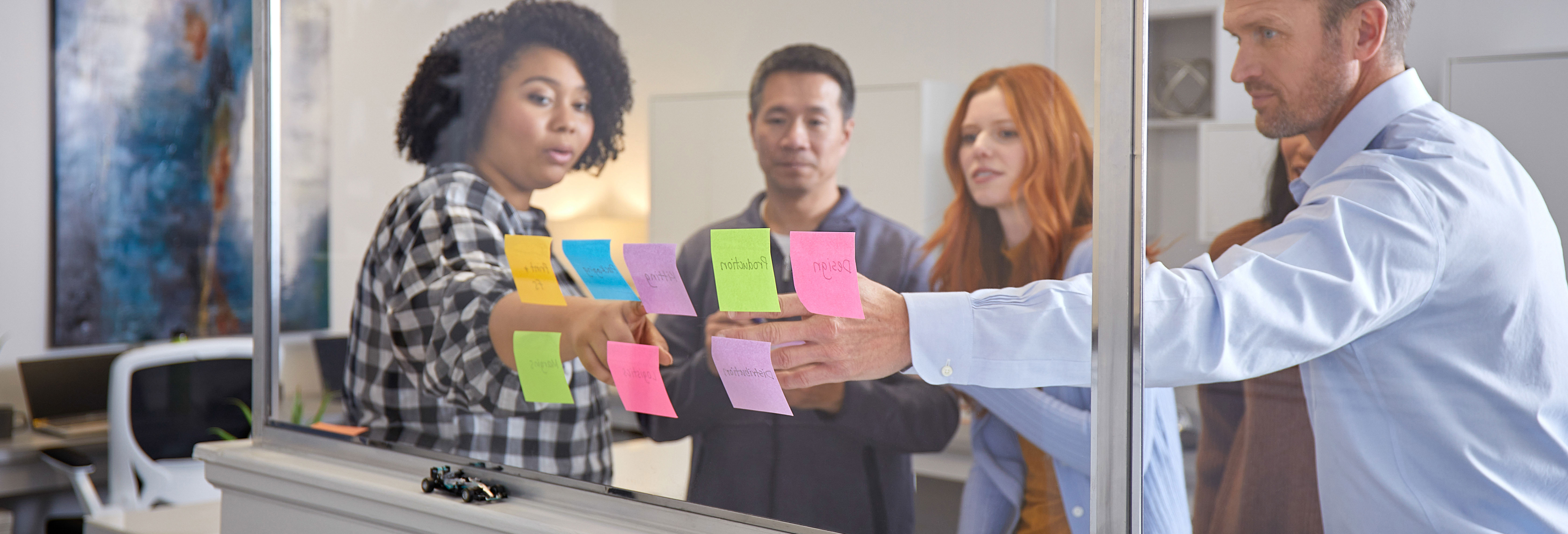 A group of five coworkers collaborating using Post-it's at a window.