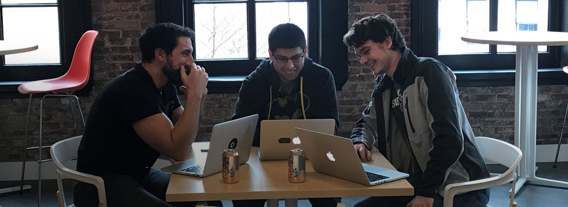 Three employees sitting at a table with their laptops collaborating